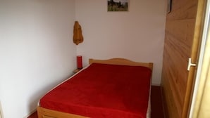 A small, single-bed room with a wooden headboard, a red bedspread, a small bedside table with a red lamp, and a wooden wardrobe. - 50m from ski slopes, balcony, parking, tv, ski locker, 30-32m², Les 7 Laux (Les Adrets)