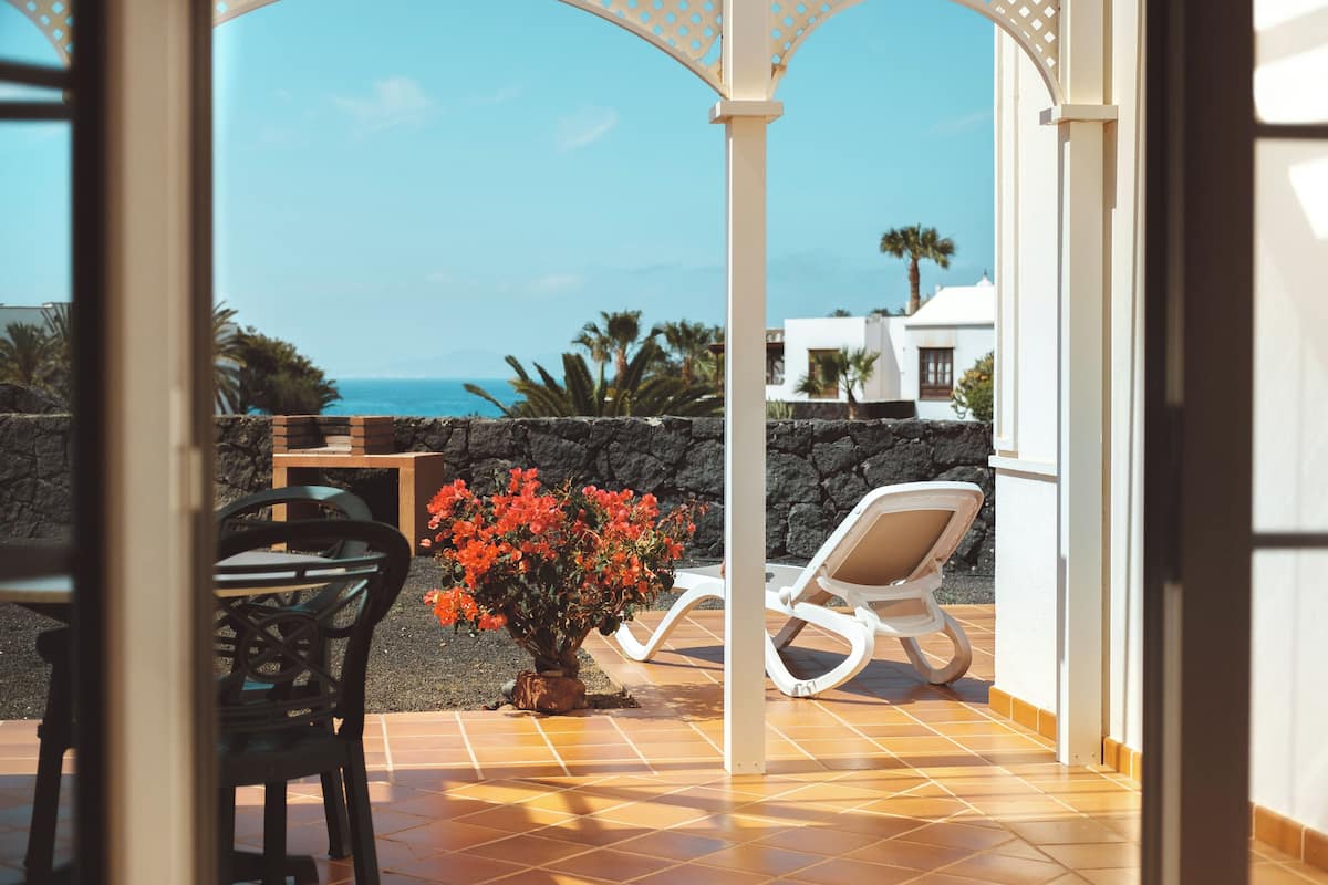 Une terrasse avec une chaise, une table et un pot de fleurs.