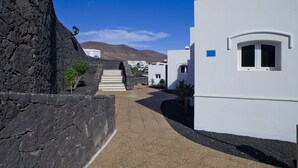 A narrow street with white buildings, a stone wall, and a mountain in the background. - Apartamentos Livvo Coloradamar (Yaiza)