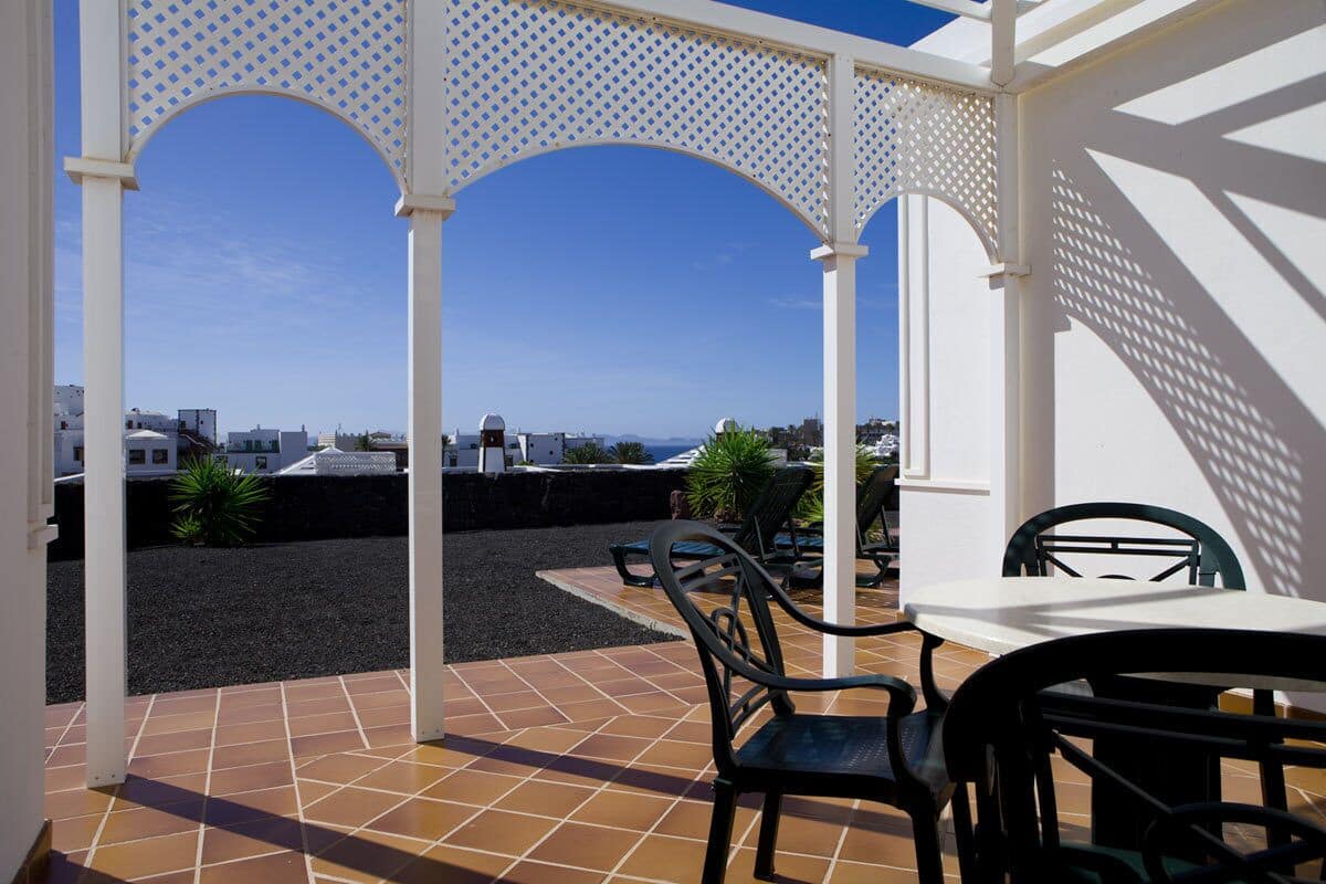 Une terrasse extérieure dotée d’une pergola blanche, de chaises noires et d’une table.