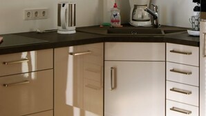 A modern kitchen with stainless steel appliances, including a kettle, coffee maker, and toaster. There are beige cabinets and a black countertop. - Fürstenhof Rügen (Sassnitz)