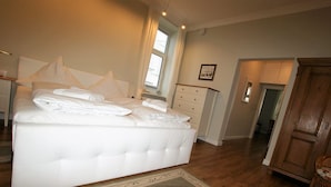 A bedroom with a large bed, a bedside table with a lamp, a dresser, and a wooden wardrobe. - Fürstenhof Rügen (Sassnitz)