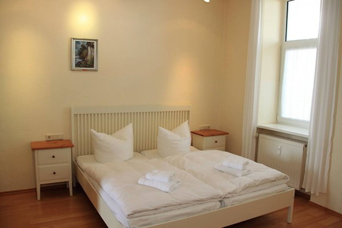 A bedroom with a double bed, two bedside tables, a radiator, and a window with curtains.