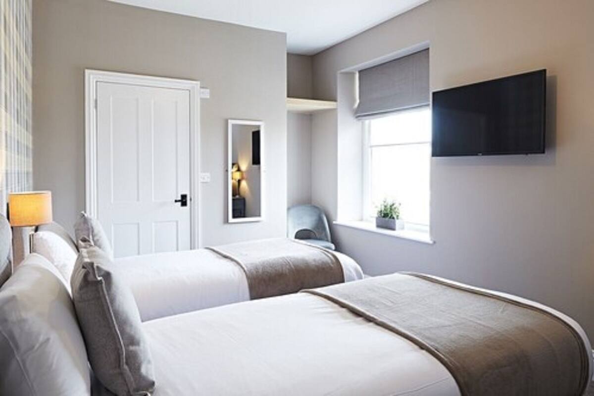 Habitación de hotel con dos camas, televisor montado en la pared, ventana con vistas y una puerta.