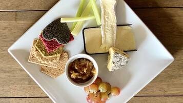 Een wit vierkant bord met diverse etenswaren, waaronder kaas, crackers, druiven en augurken, op een houten tafel.