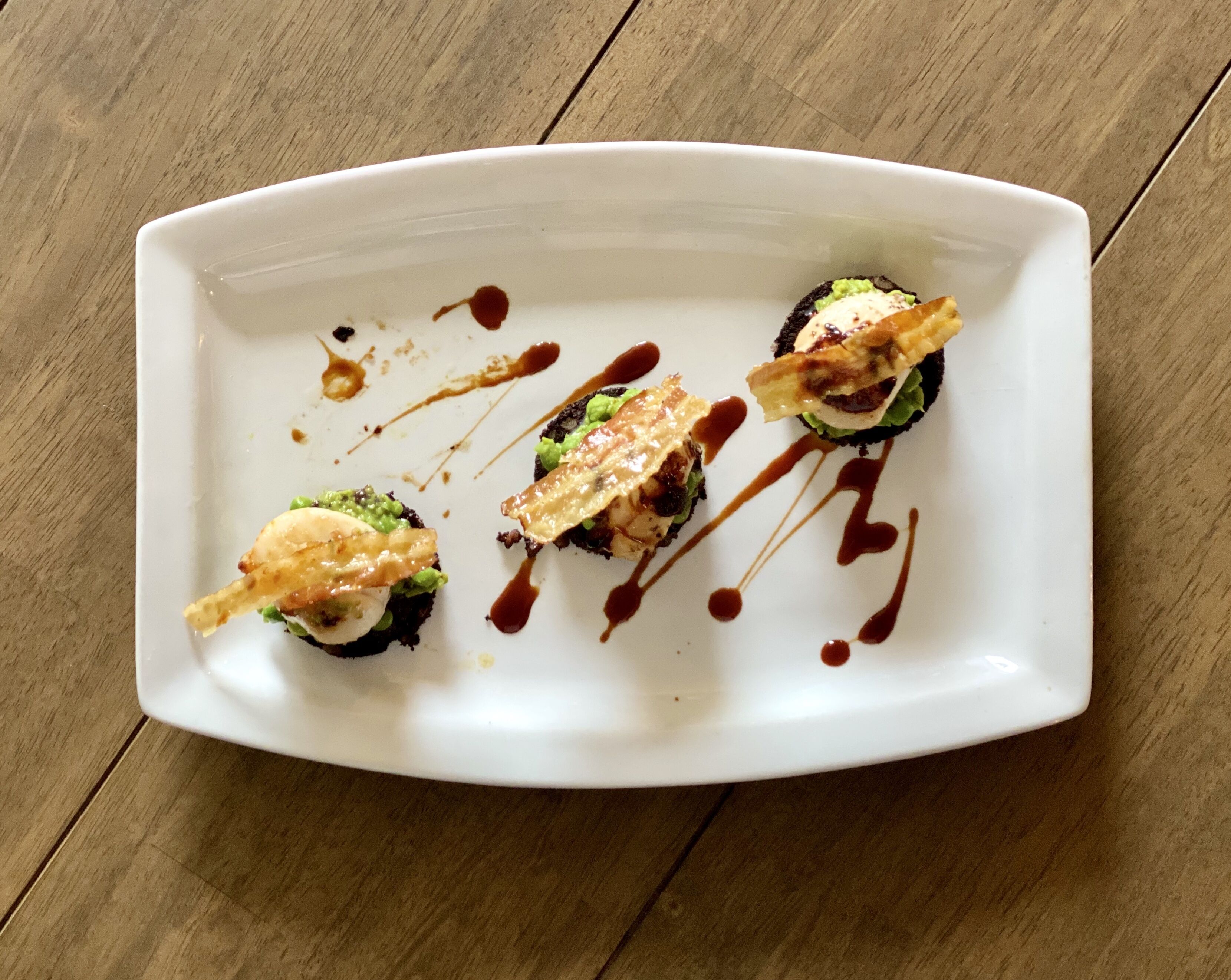 En vit, rektangulär tallrik med tre sushibitar, var och en toppad med en skiva fisk och garnerad med sås.