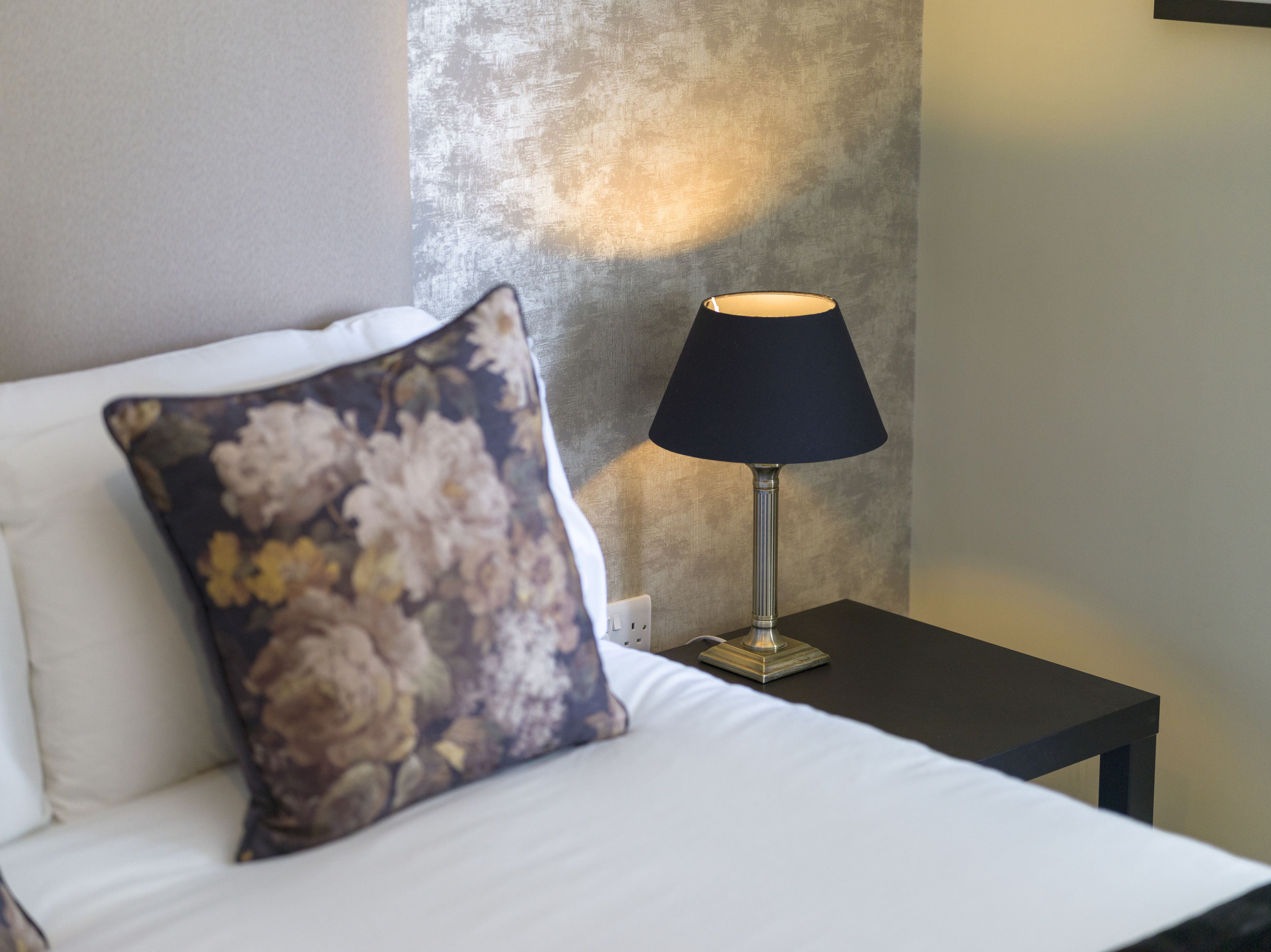 A neatly made bed with a floral pillow and a table lamp beside it.