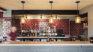 Een bar met een bakstenen muur, hangende hanglampen en een toonbank met verschillende flessen en glazen.