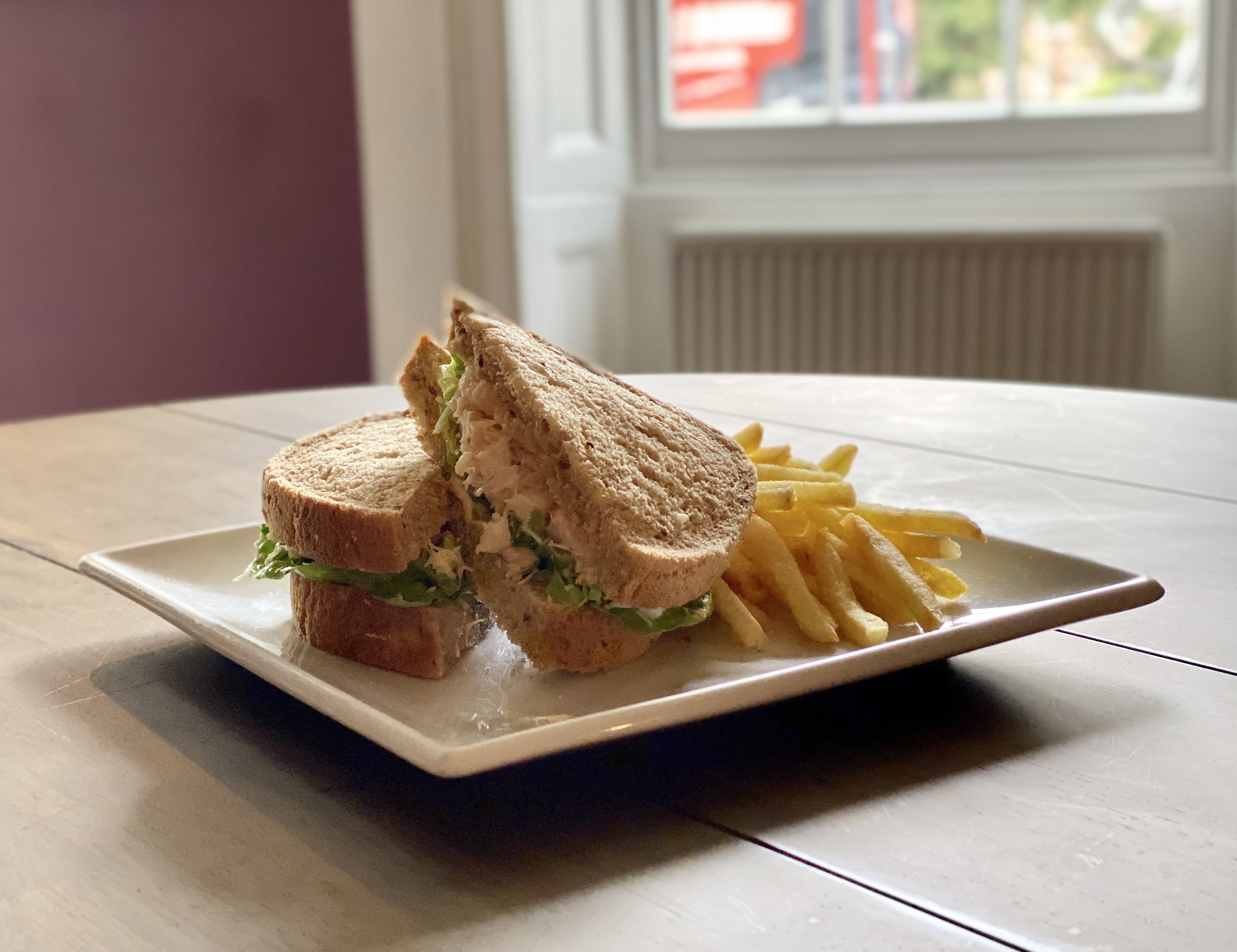 A sandwich and fries on a white plate on a wooden table.