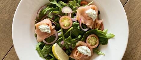 A white bowl of salad with spinach, sliced tomatoes, red onions, and smoked salmon, garnished with a lemon wedge.