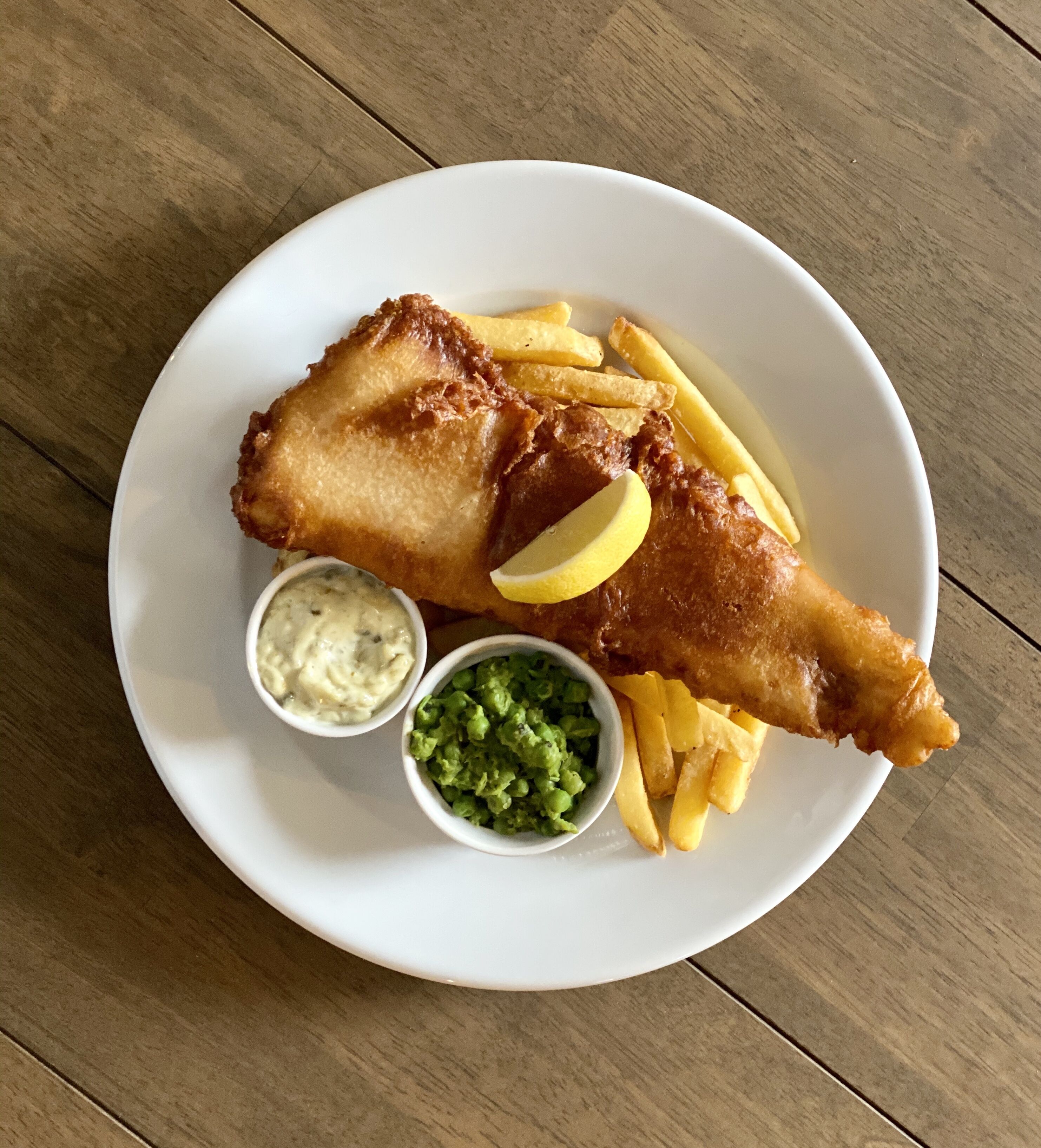 A plate of fish and chips with lemon wedges and two side dishes of mushy peas and tartar sauce.