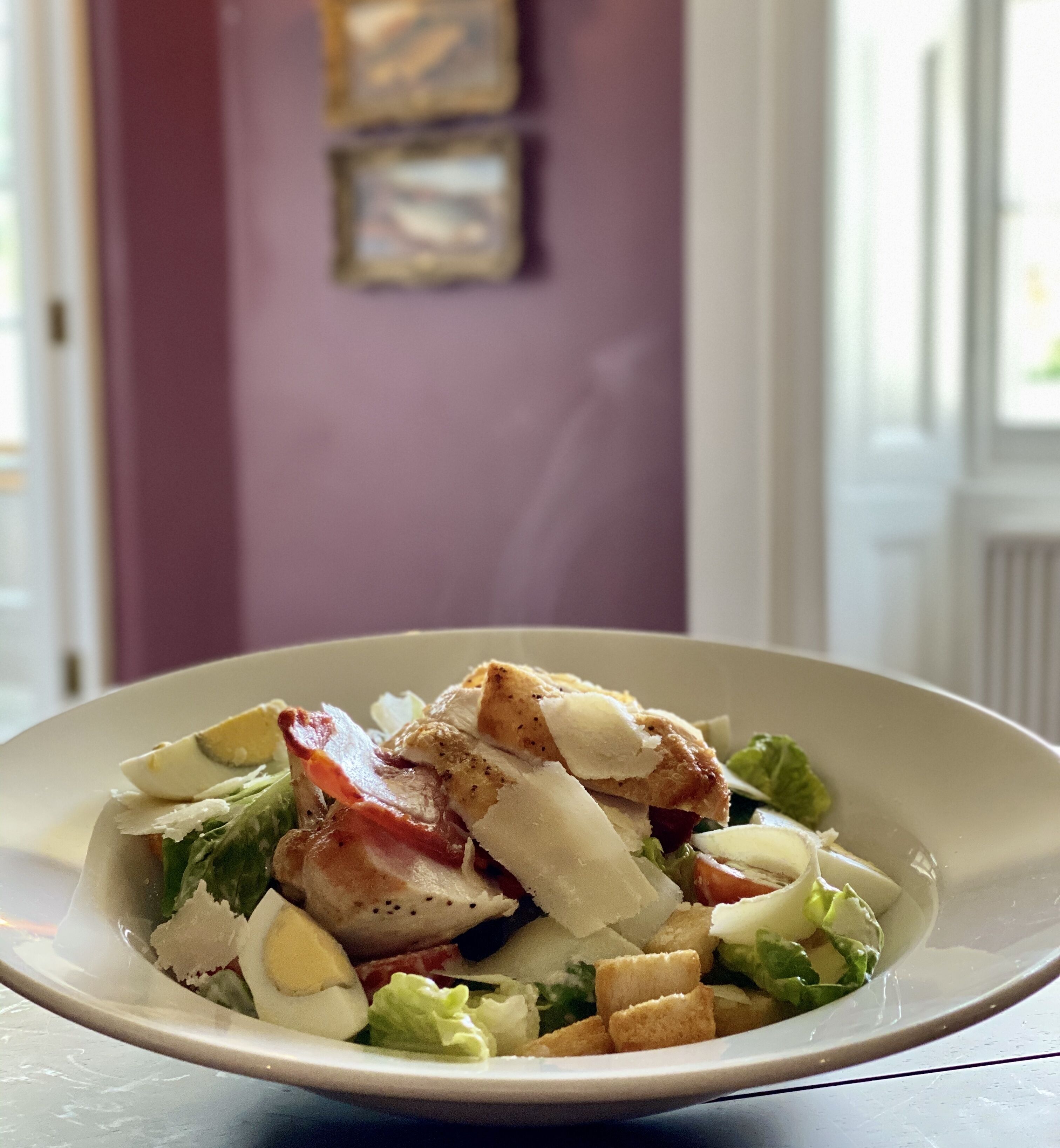 Un piatto di cibo con un'insalata, composta da lattuga, crostini e un pezzo di carne.