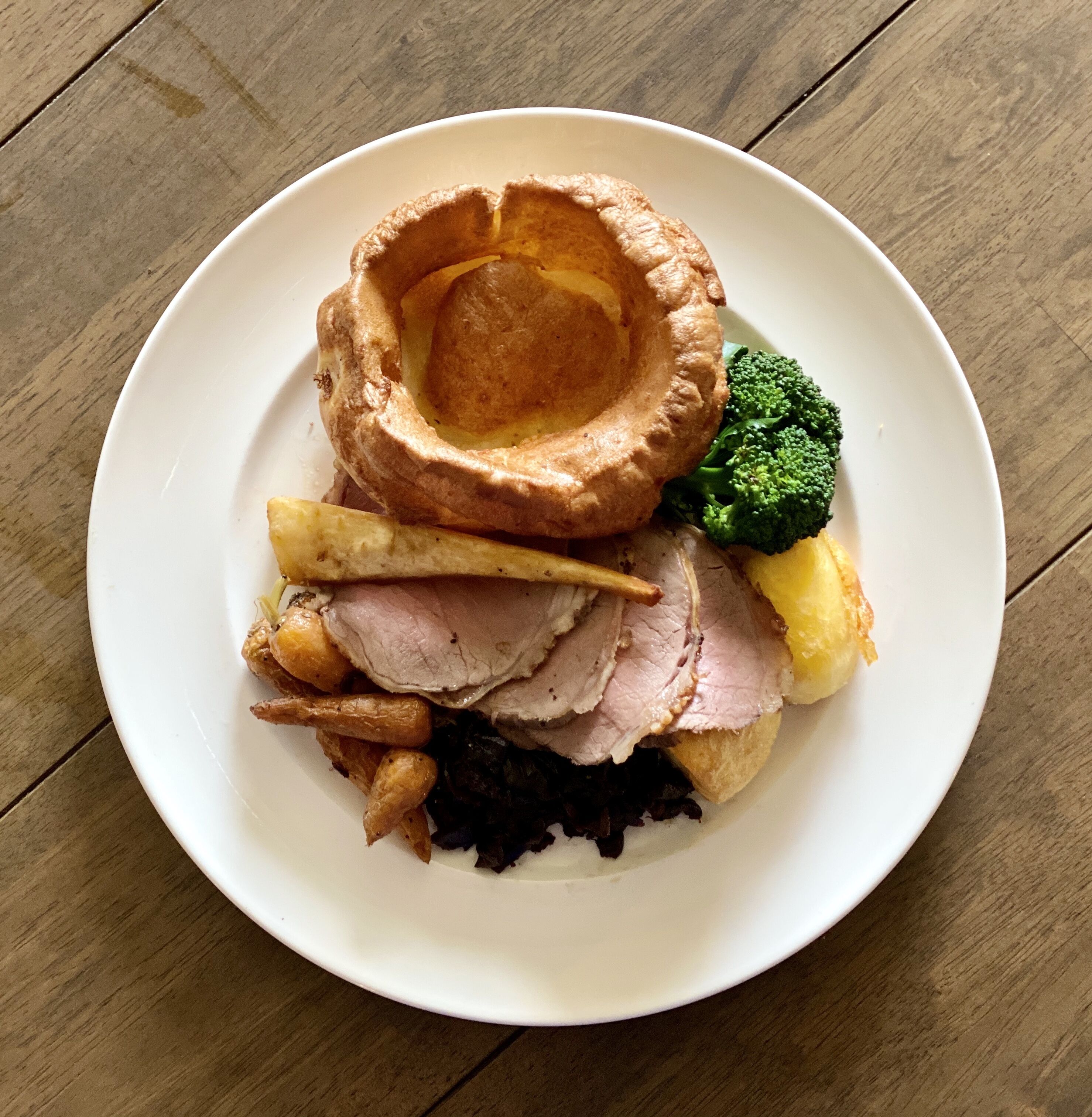 Um prato com rosbife, pudim yorkshire, acompanhamentos de pudim yorkshire e brócolis.