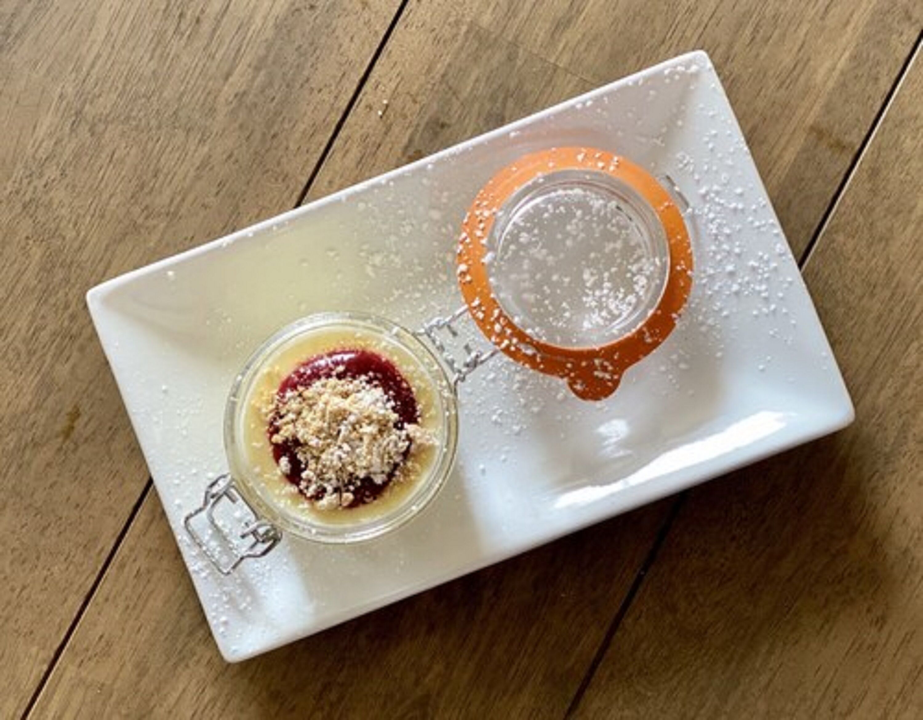 Un bocal en verre muni d’un fermoir métallique, posé sur une assiette rectangulaire blanche, elle-même placée sur une surface en bois.