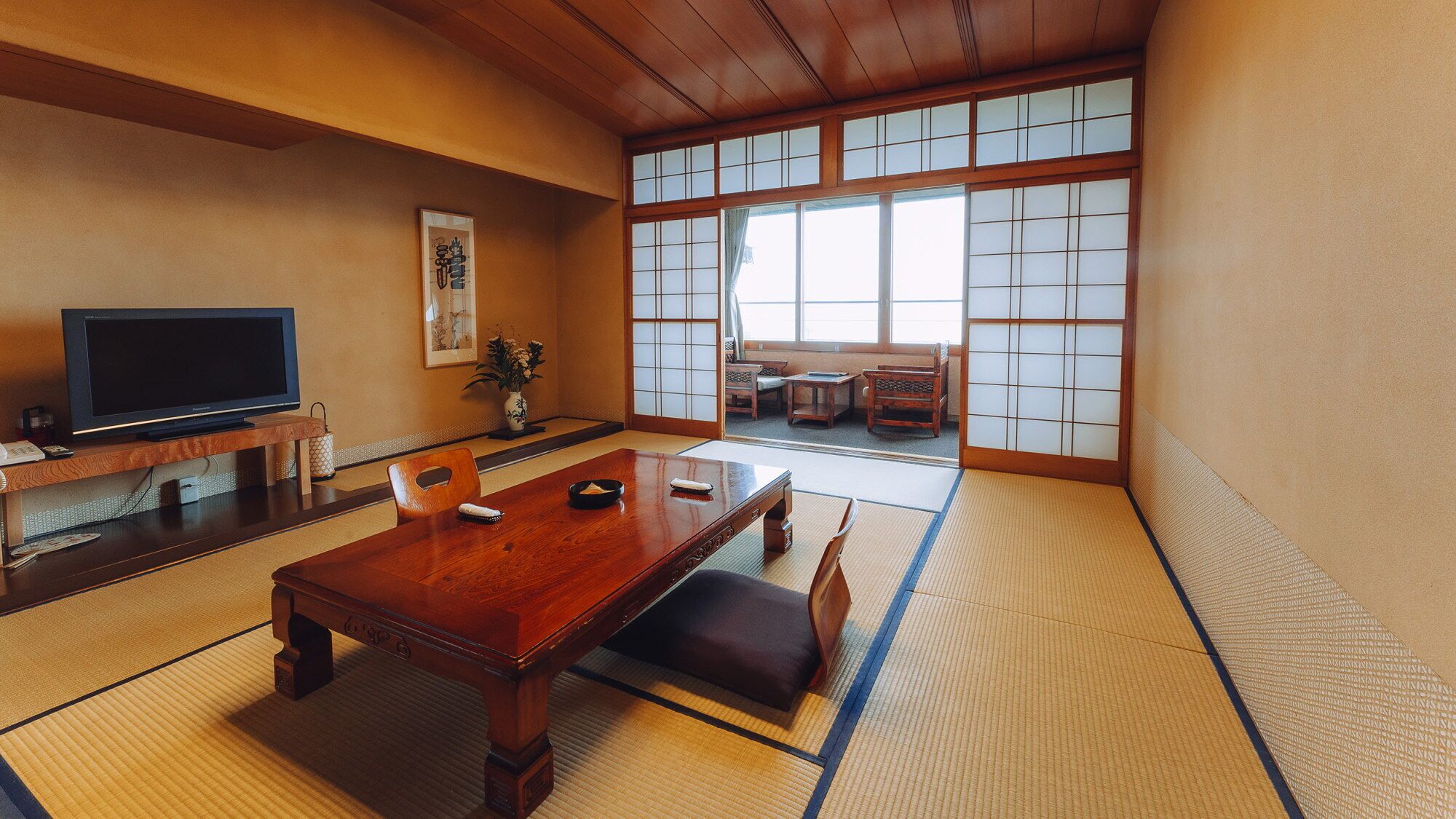 A traditional Japanese room with tatami flooring, a wooden table, a television, and sliding doors.