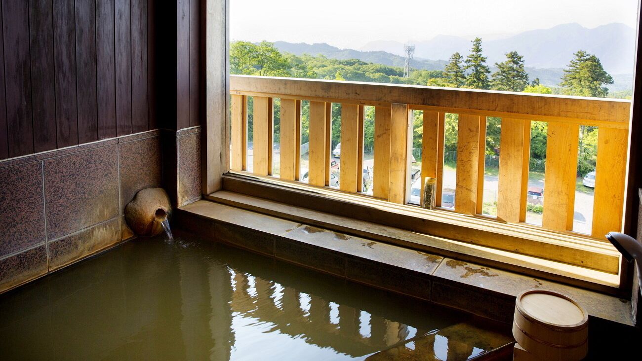 A traditional Japanese onsen with a wooden railing, a stone wall, and a view of a parking lot and mountains.