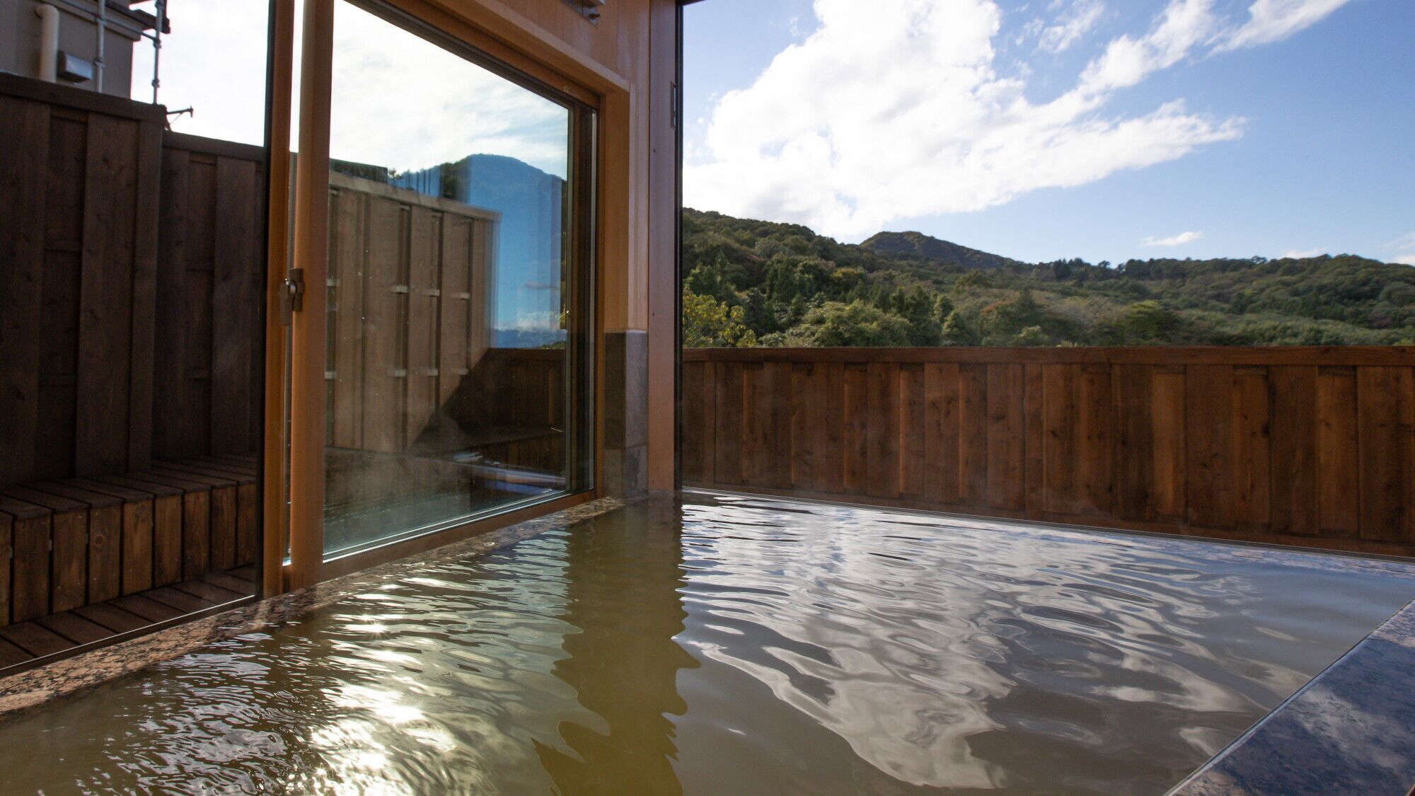A hot tub area with a wooden deck and a glass wall offering a view of a mountainous landscape.