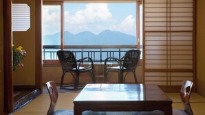 Ein Zimmer mit Tatami-Boden, einem niedrigen Tisch, zwei Stühlen, Blick auf Berge durch ein großes Fenster und einem Shoji-Bildschirm.