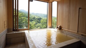 Ein Wellnessraum mit einer großen Badewanne, Holzwänden und Blick auf einen bewaldeten Berg.