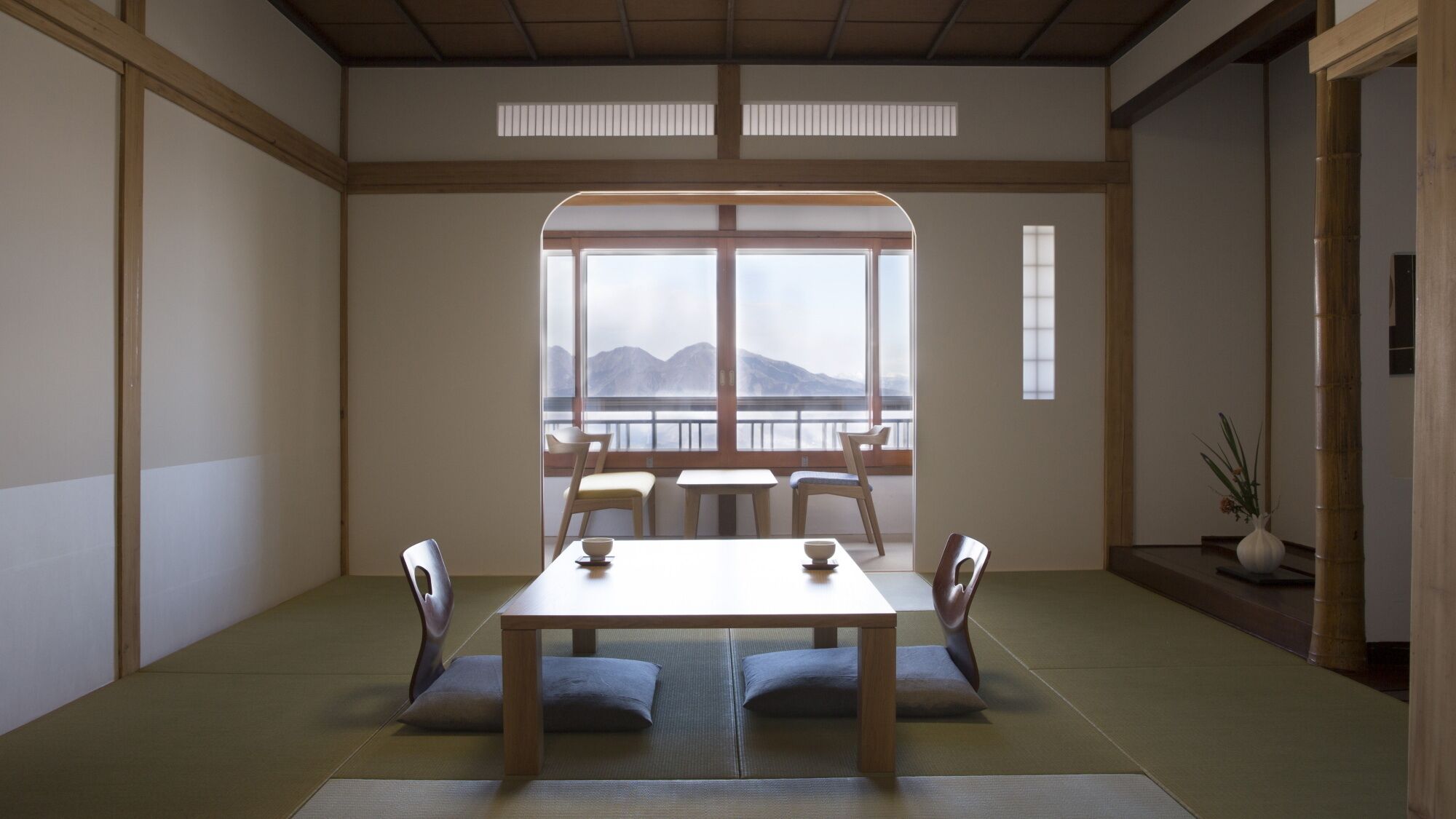 A traditional Japanese room with tatami flooring, a low table, and a view of mountains through large windows.