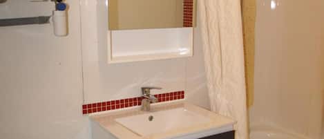 A bathroom with a toilet, sink, mirror, and shower.