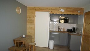 A compact kitchen with wooden walls, a microwave, a sink, and a small dining area with stools. - 50m from ski slopes, balcony, parking, tv, ski locker, 28m², Les 7 Laux (Les Adrets)