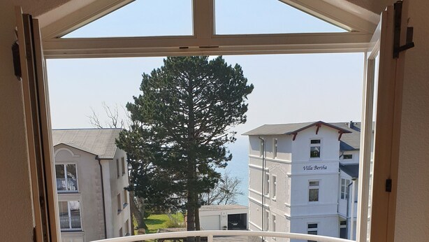 Un balcón con una mesa y dos sillas, una terraza de madera y vistas a edificios cercanos.