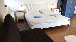 Un dormitorio con una cama, una mesita de noche, una estantería, un sofá y una pequeña mesa.