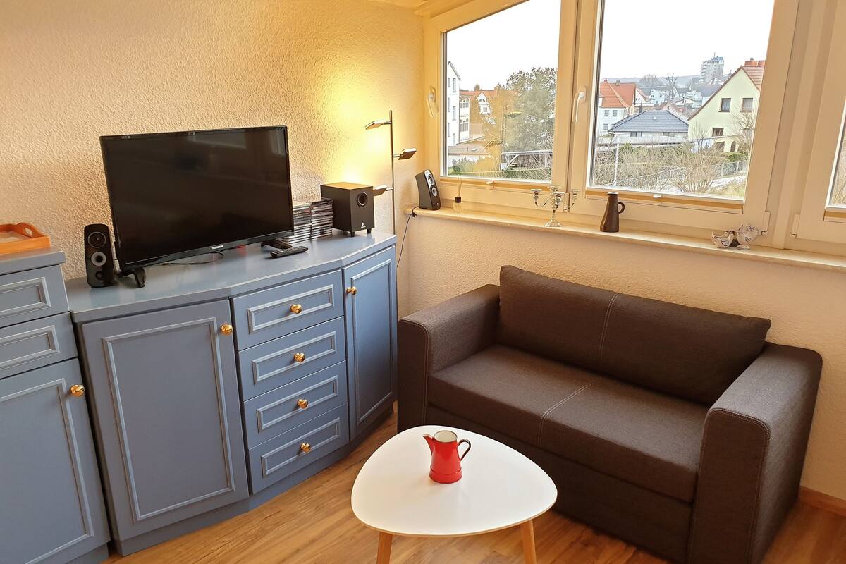 Un espacio habitable compacto con un armario gris, un televisor de pantalla plana, una cafetera roja y un sofá marrón.