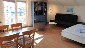 Un salón acogedor con un sofá, una mesa de comedor con sillas, una estantería y un televisor.