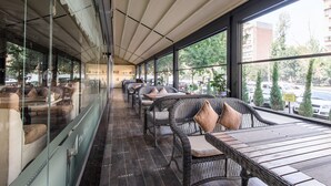 A cafe with wicker furniture, large windows, and a view of the street. - The Royal Mezbon Hotel & SPA (Tashkent)
