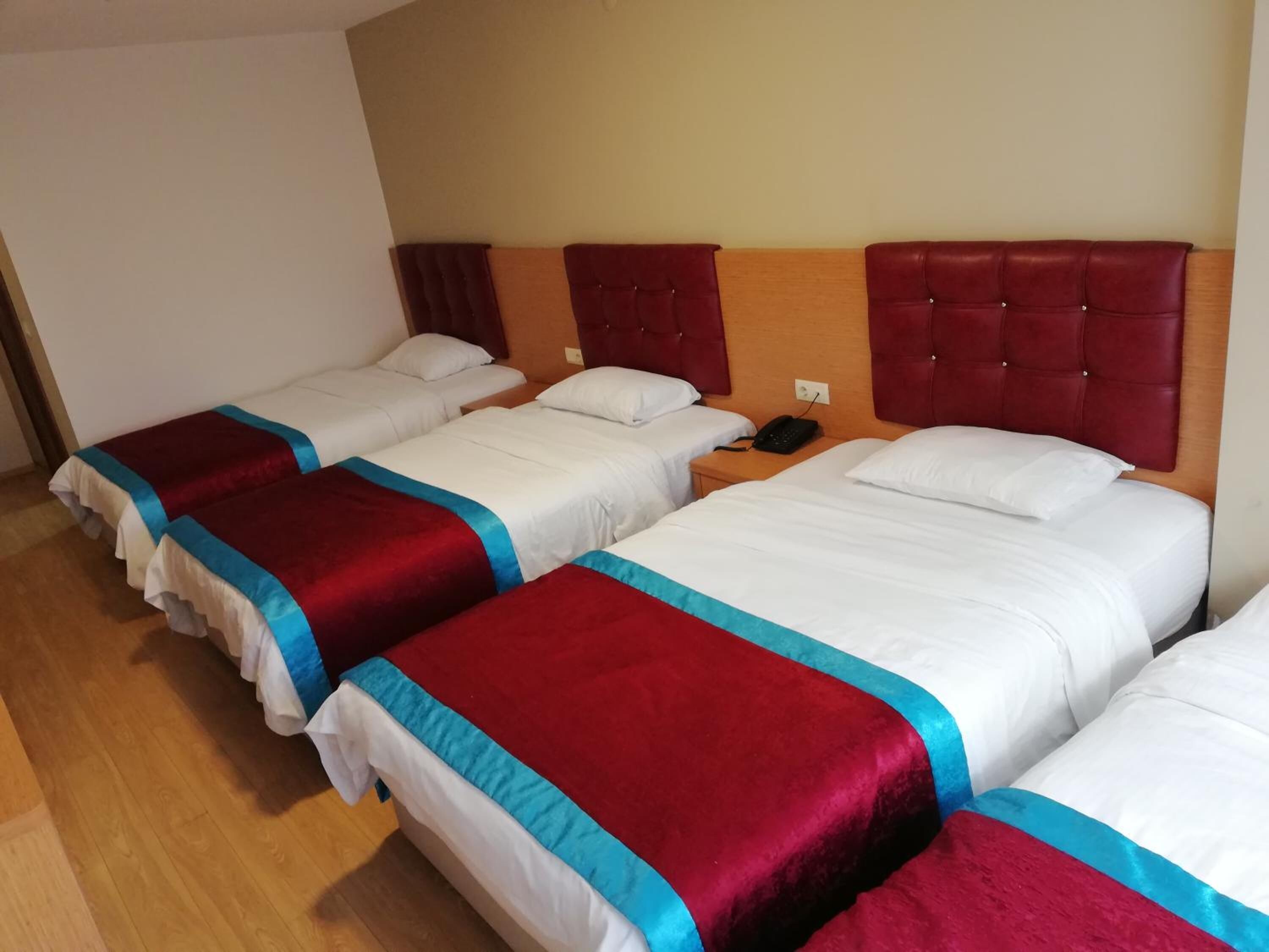 Habitación de hotel con cuatro camas dispuestas en fila, cada una con cabecero rojo y ropa de cama blanca.