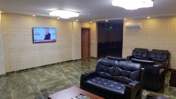 A conference room with a television screen, black leather sofas, a wooden table, and patterned walls.
