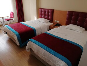 Habitación de hotel con dos camas, cada una con cubrecama rojo y azul, cabecero de madera y mesita de noche con un teléfono.