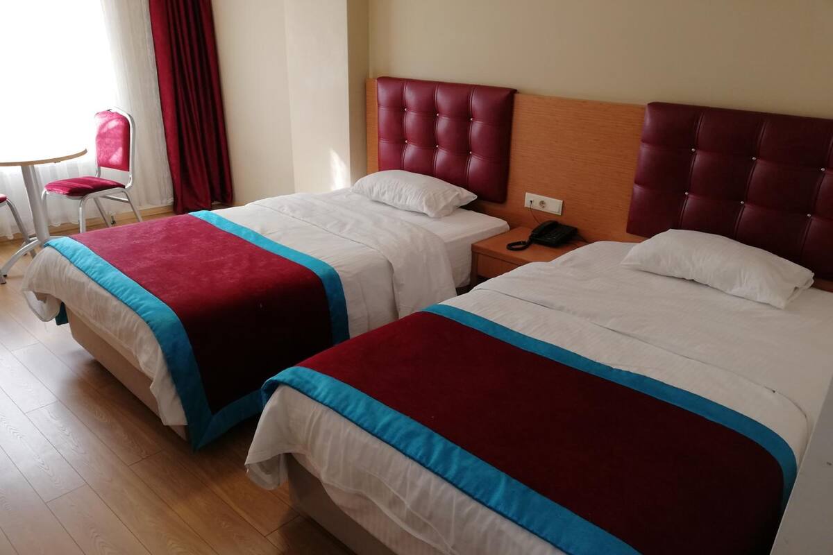 Two beds with red and blue bedspreads, a wooden headboard, a bedside phone, and a red chair.