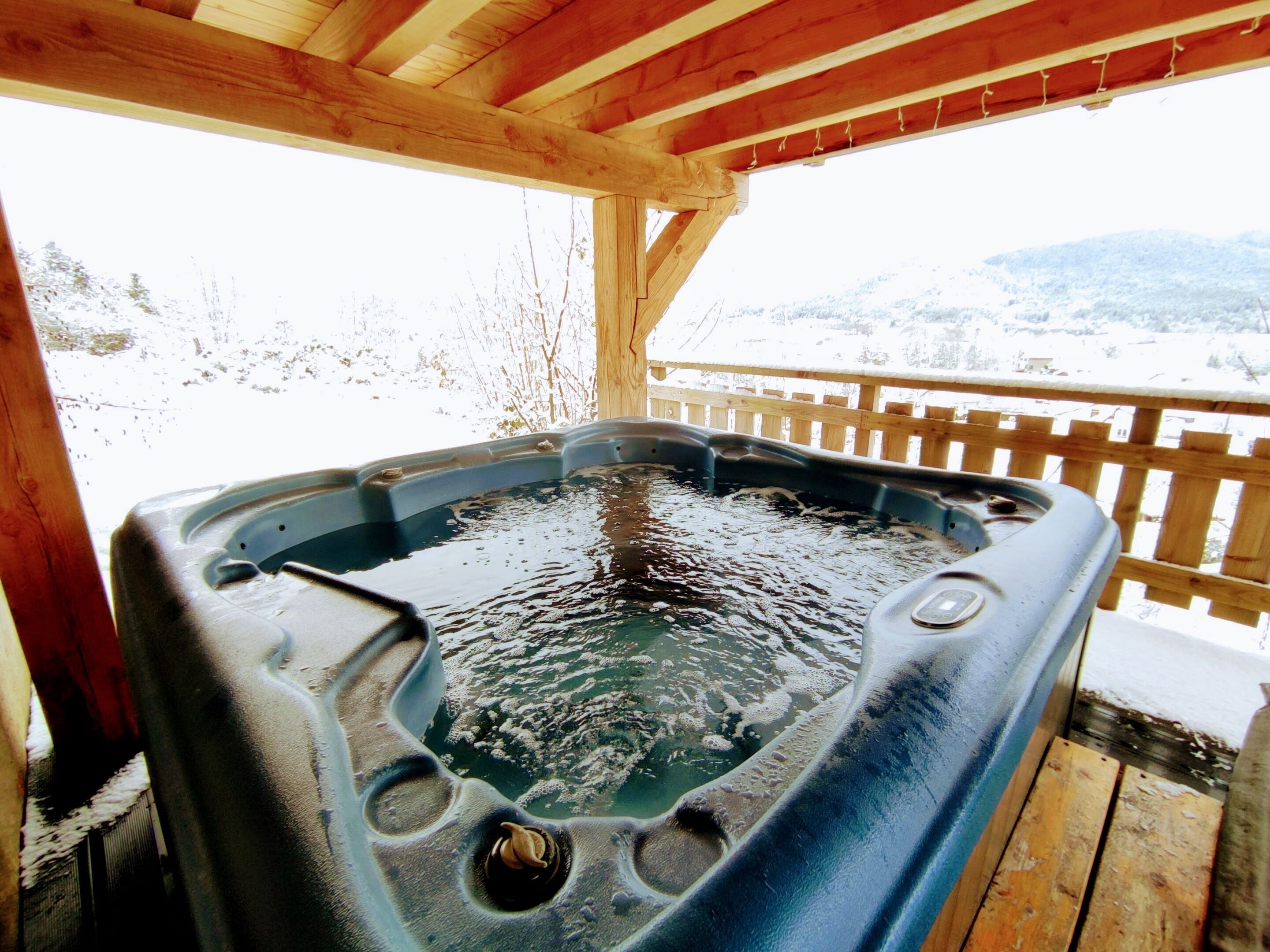 A hot tub with a wooden deck and a view of a snowy landscape.