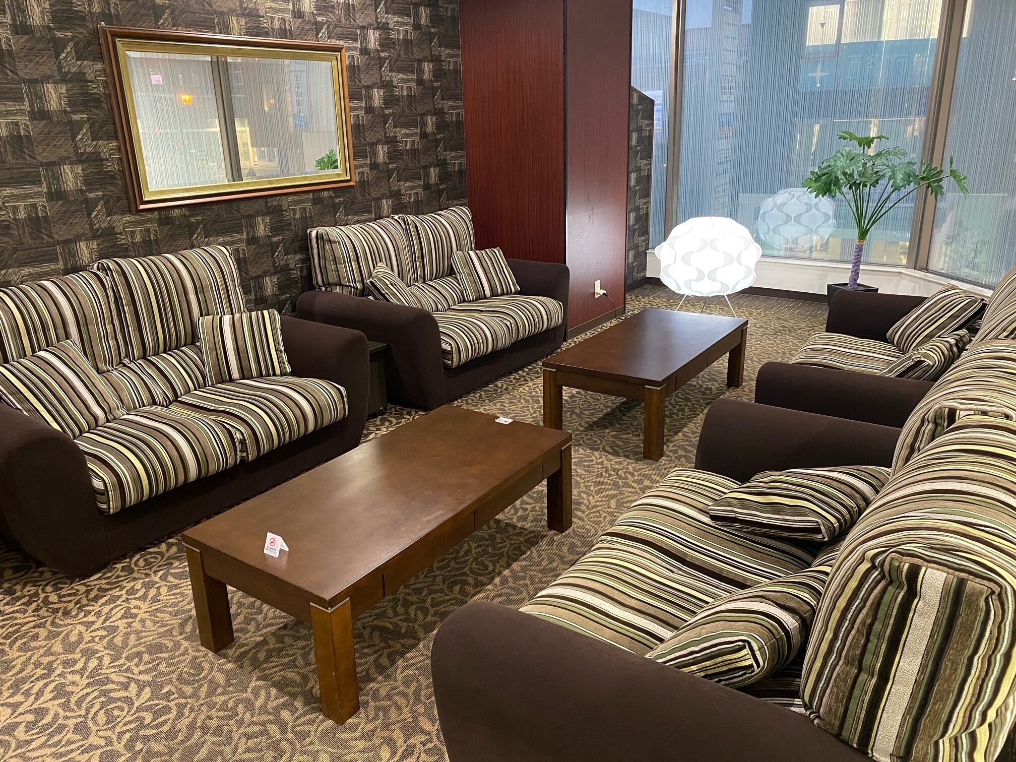 A modern living room with striped sofas, a wooden coffee table, and a large window with a city view.