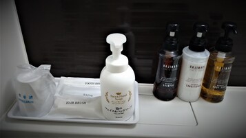 A tray with a hair brush, a bottle of face and hand soap, and three bottles of body soap on a window sill.