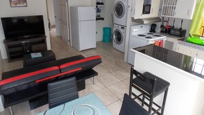 Um espaço compacto para viver, com sofá, televisão, máquina de lavar, cozinha pequena equipada com fogão e área de jantar.