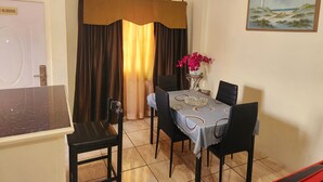 Uma sala de jantar com mesa posta para quatro pessoas, um vaso com flores e um quadro na parede.