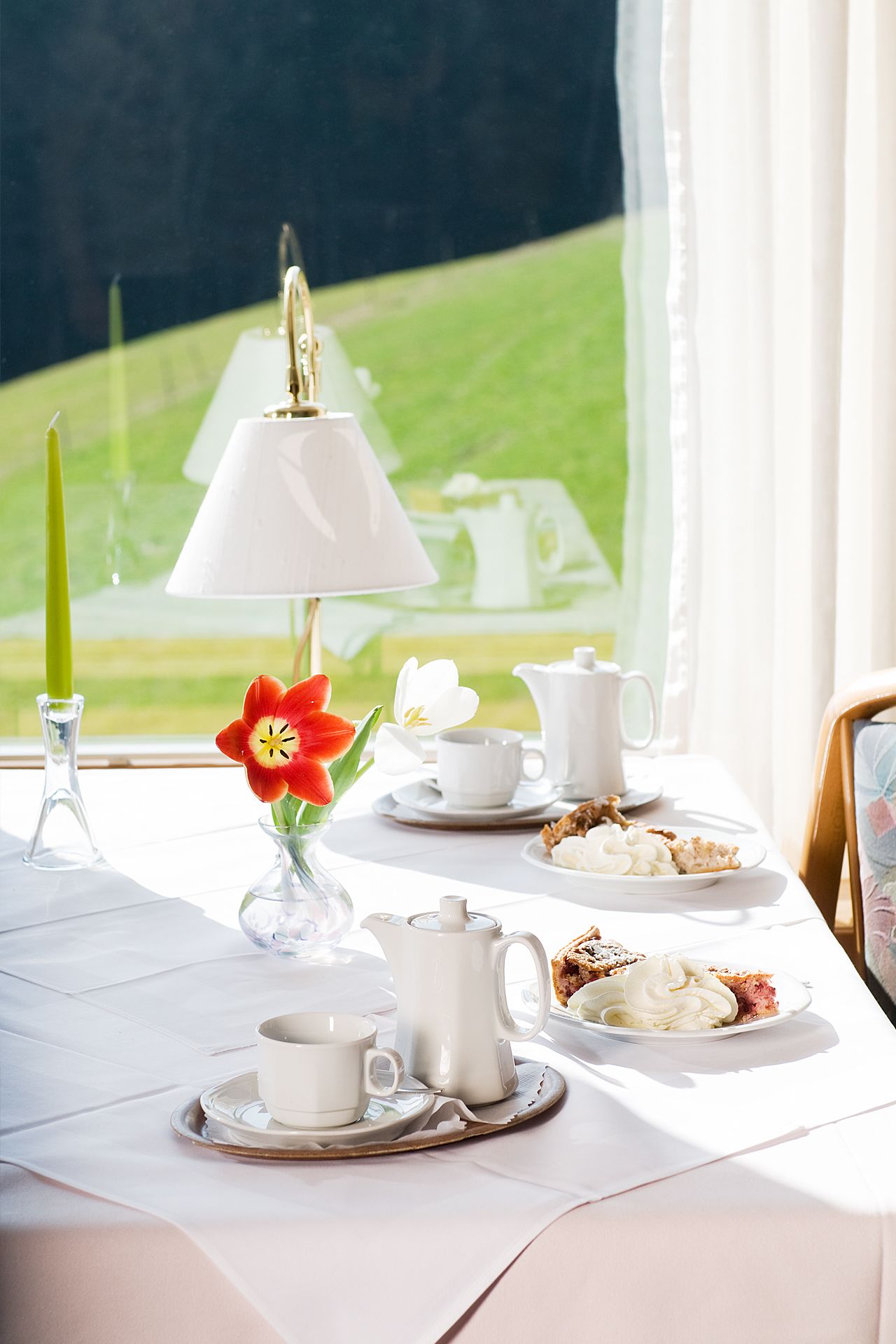 A table set for tea with a white teapot, cups, and a plate of pastries.
