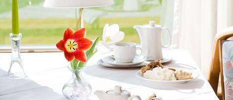 A table set for tea with a white teapot, cups, and a plate of pastries.