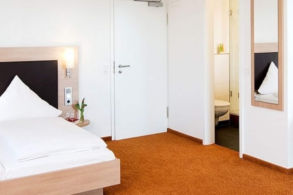 Quarto de hotel com uma cama, uma cadeira, uma mesa pequena com frutas e uma televisão.