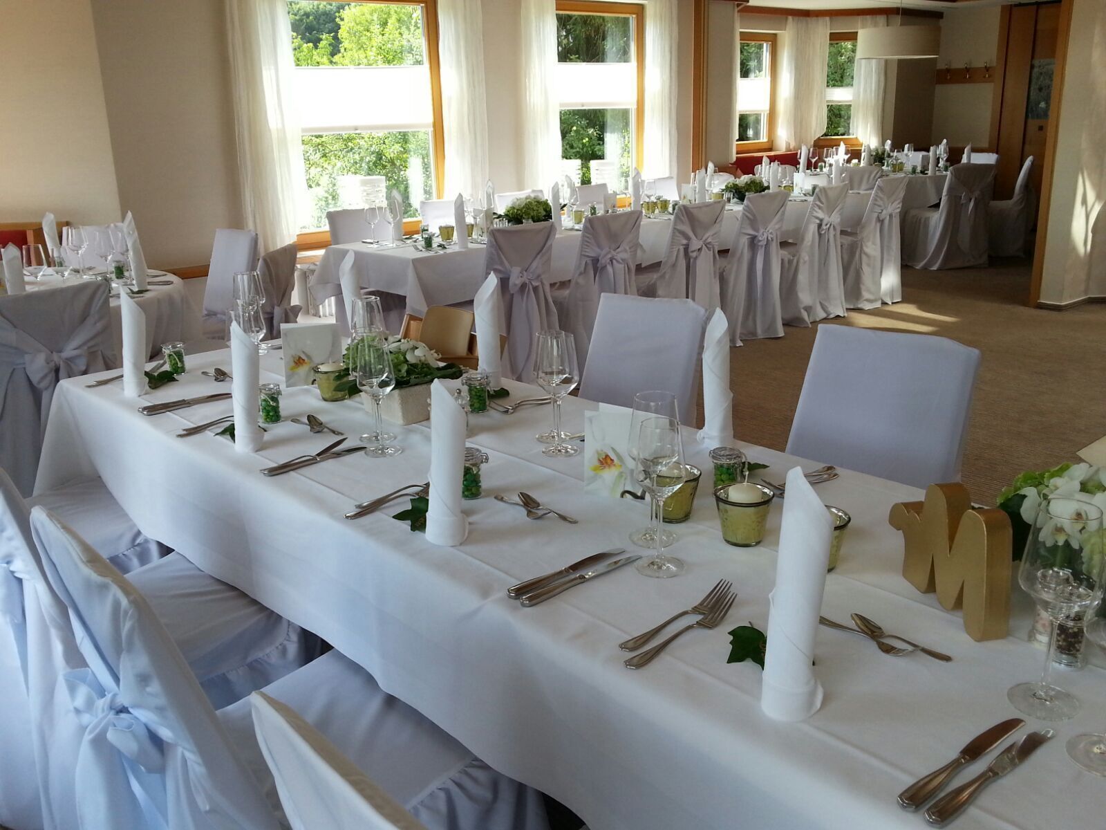 A banquet hall with long tables set for a formal event, featuring white tablecloths, neatly arranged silverware, and candle centerpieces.