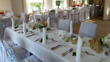 Un salón de banquetes con largas mesas dispuestas para un evento formal, con manteles blancos, cubertería impecable y centros de mesa con velas.