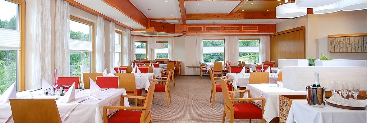 Un restaurante con varias mesas y sillas, ventanas amplias y vistas a zonas verdes.