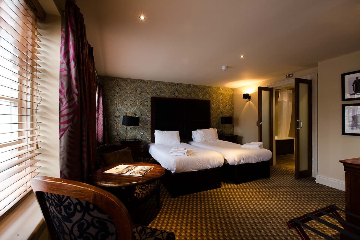 A hotel room with two beds, a desk, a chair, a patterned carpet, and a large mirror.