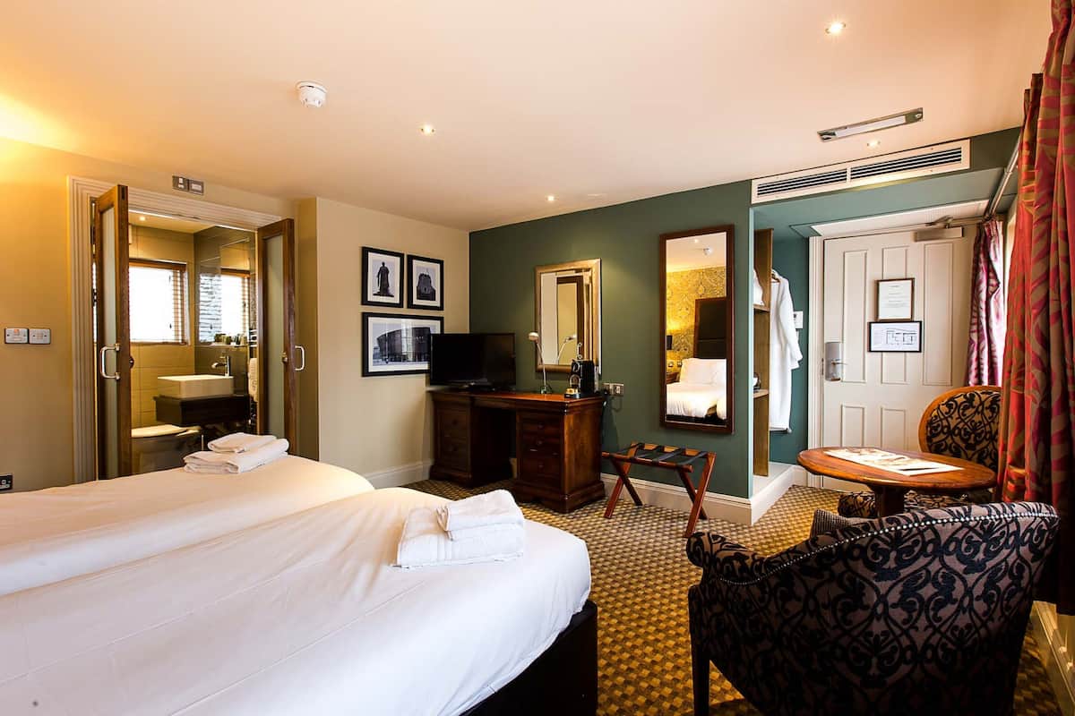 A hotel room with two beds, a desk, a chair, a television, a mirror, and a bathroom.