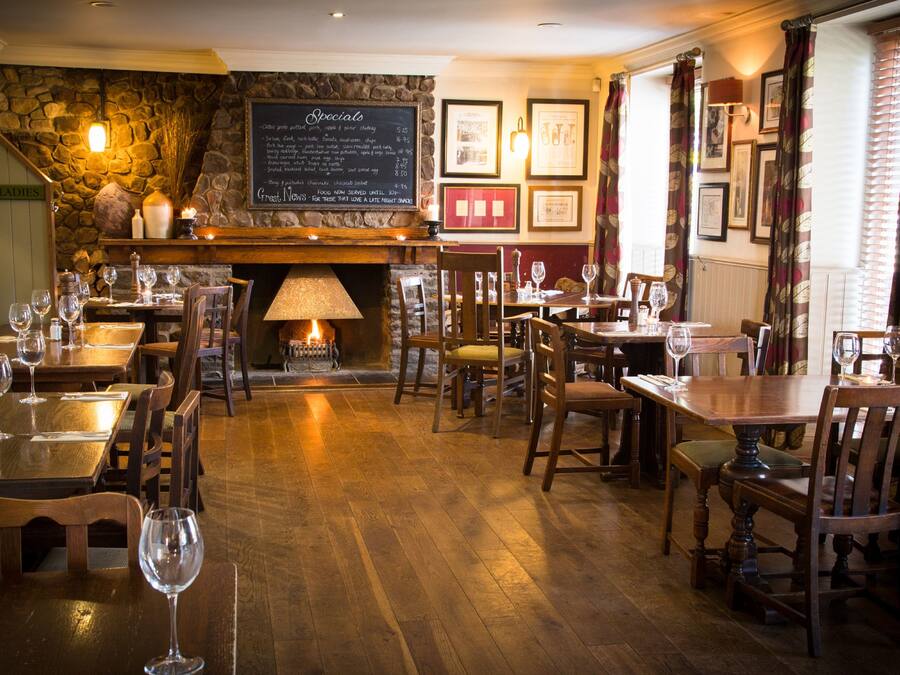 Un restaurant chaleureux avec des tables et des chaises en bois, un mur en pierre, une cheminée et des tableaux encadrés accrochés au mur.