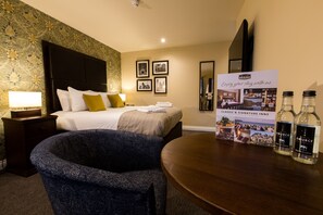 A hotel room with a bed, a nightstand, a chair, a table, and a poster advertising the hotel.